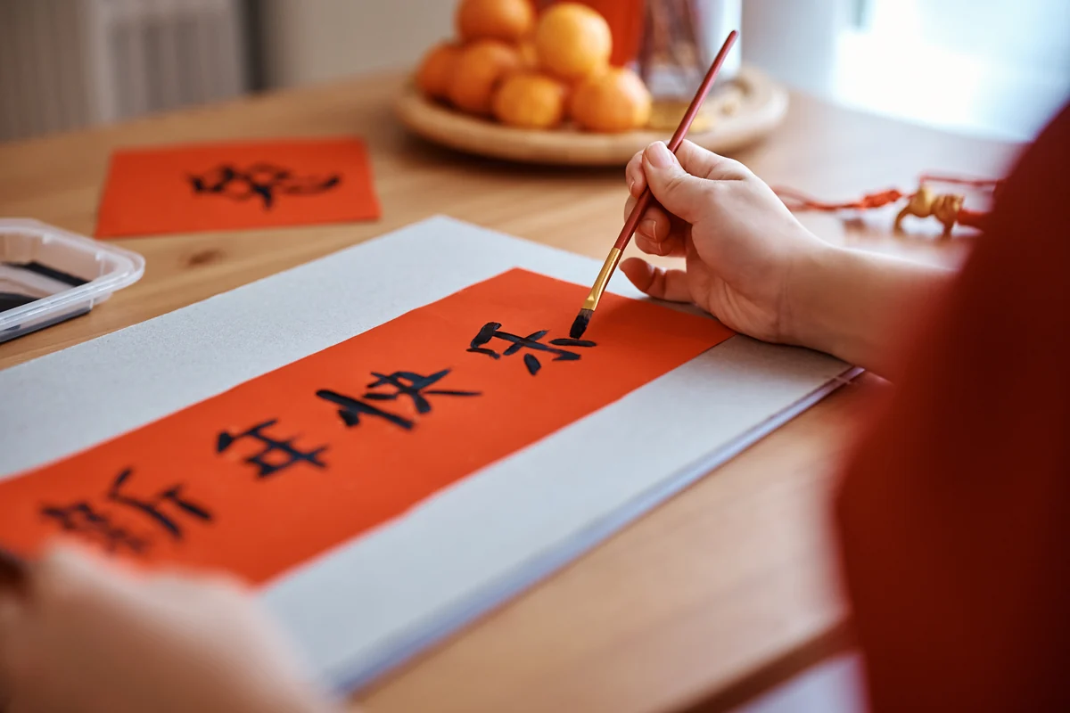 Traveler practicing Chinese calligraphy with a brush on red paper at a table in Beijing.