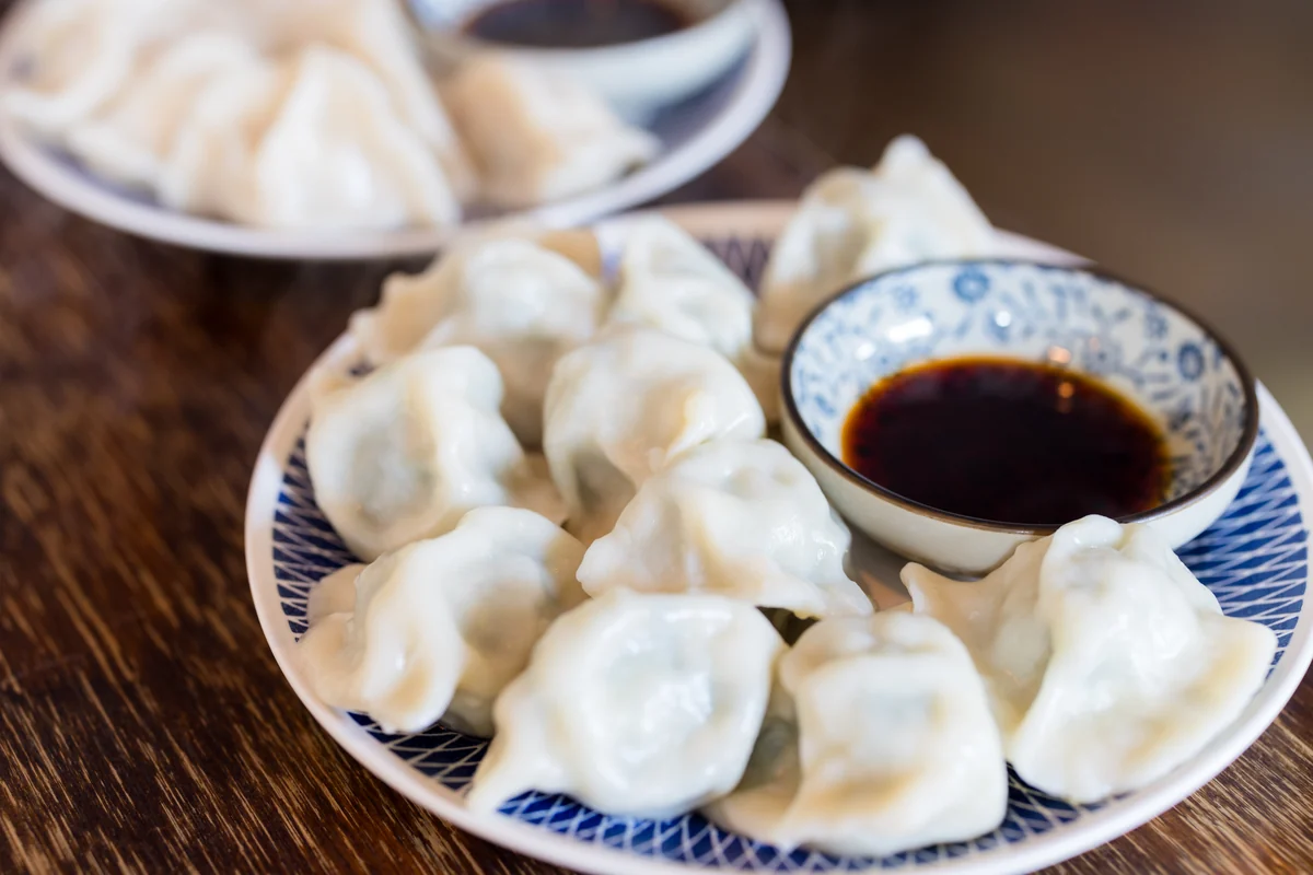 Plate of boiled dumplings with dipping sauce on a wooden table in Beijing.