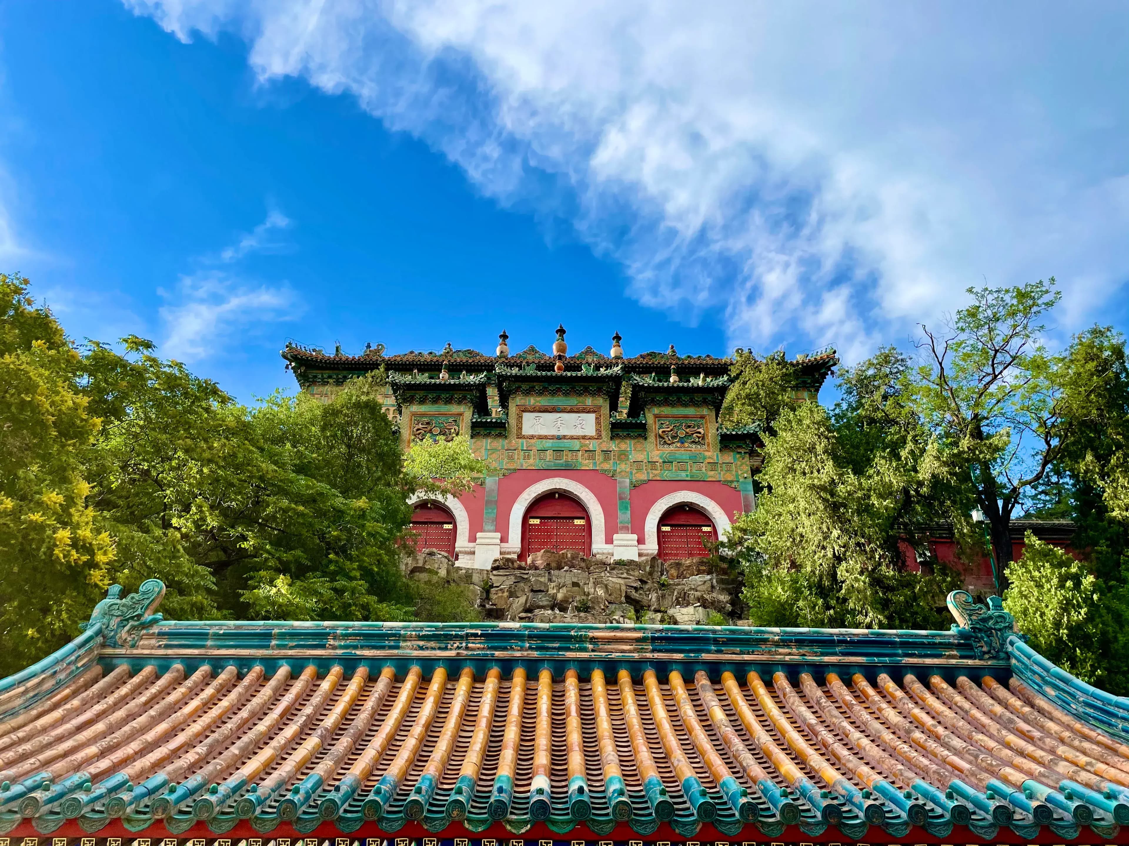 A traditional Chinese building with a colorful, ornate roof and intricate details, surrounded by lush greenery under a bright blue sky.