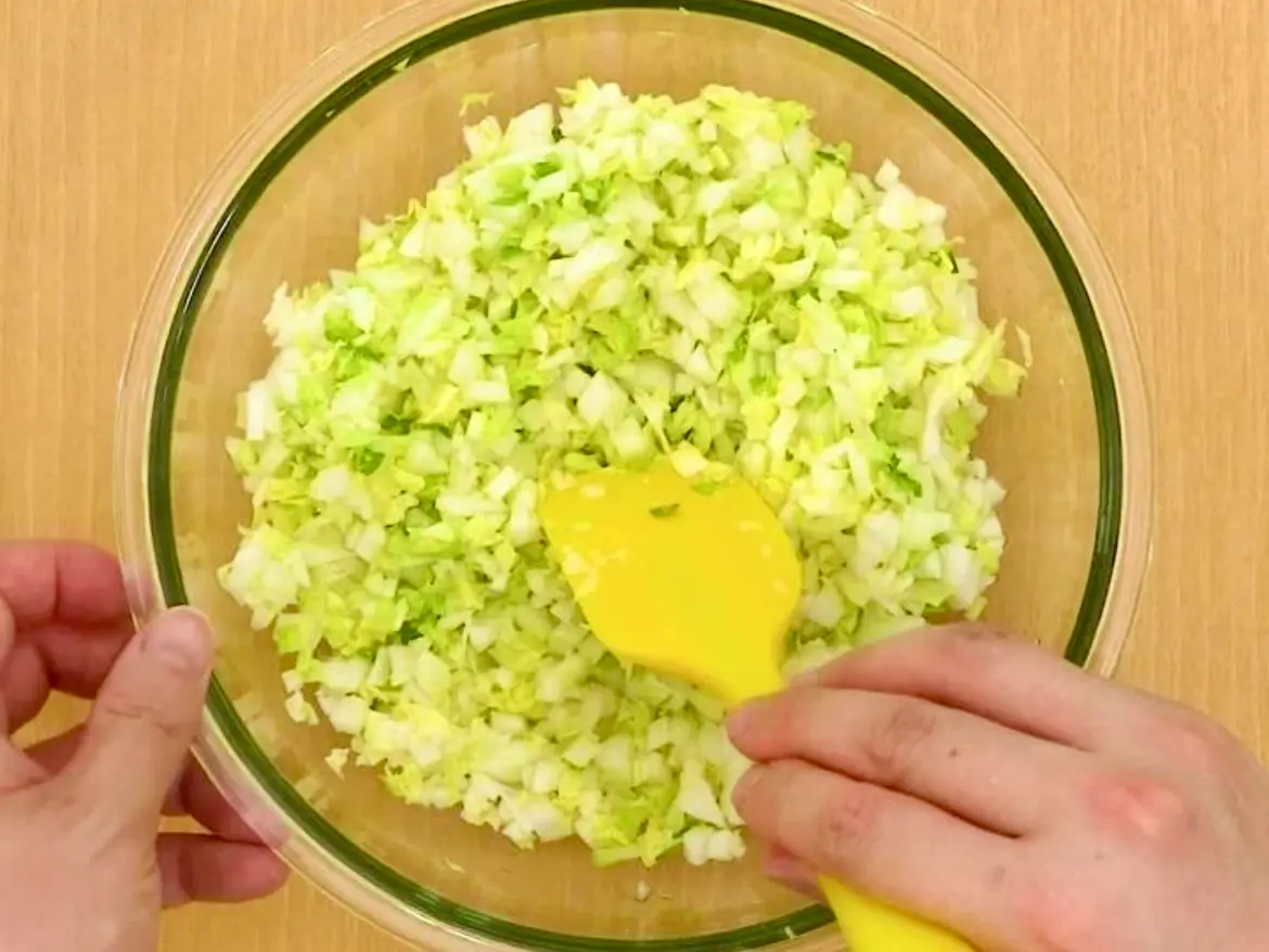 Finely chopped Napa cabbage being mixed in a bowl