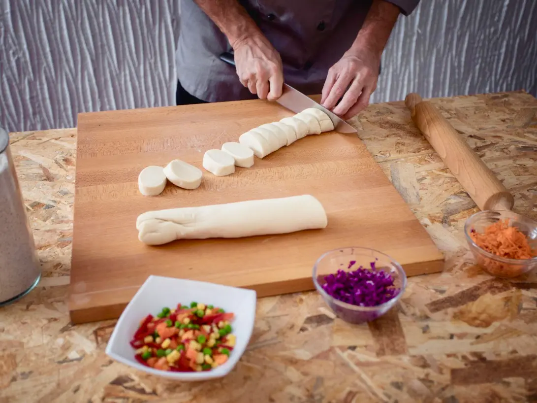 A chef cutting dumpling dough into small pieces on a wooden board
