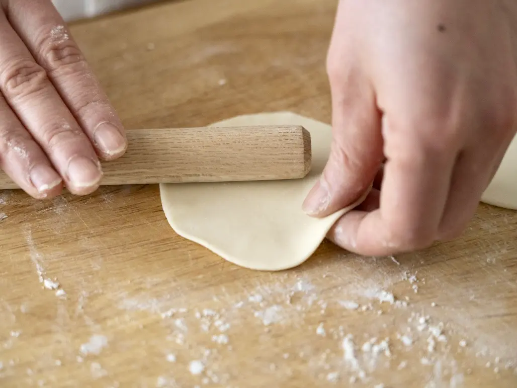 Hands rolling out dumpling wrappers on a wooden surface
