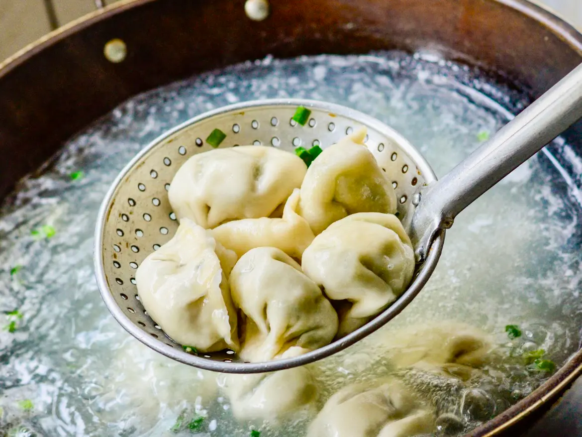 Cooked dumplings in a strainer over a pot of boiling water