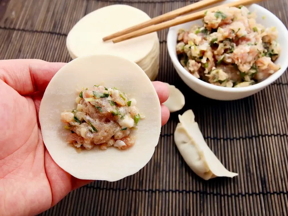 A dumpling wrapper with pork and napa cabbage filling in the center
