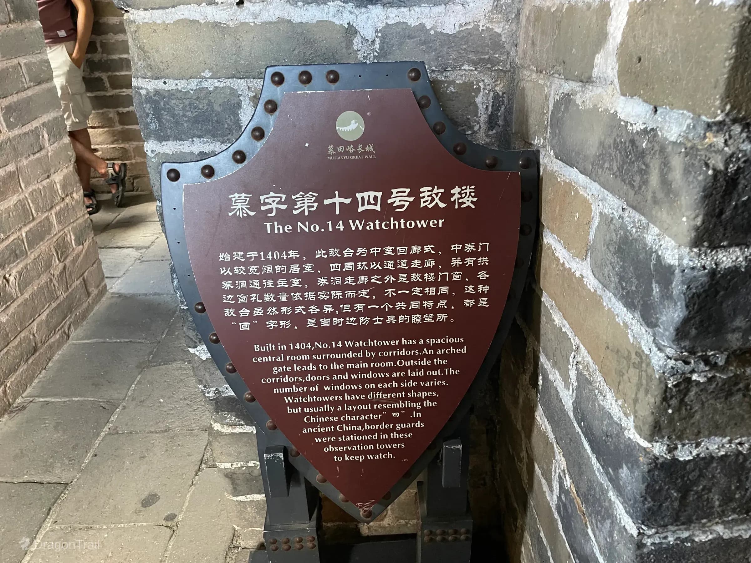 Shield-shaped bilingual Mutianyu plaque titled The No. 14 Watchtower, describing the 1404 tower’s 回-shaped layout, mounted on a riveted stand inside a brick corridor