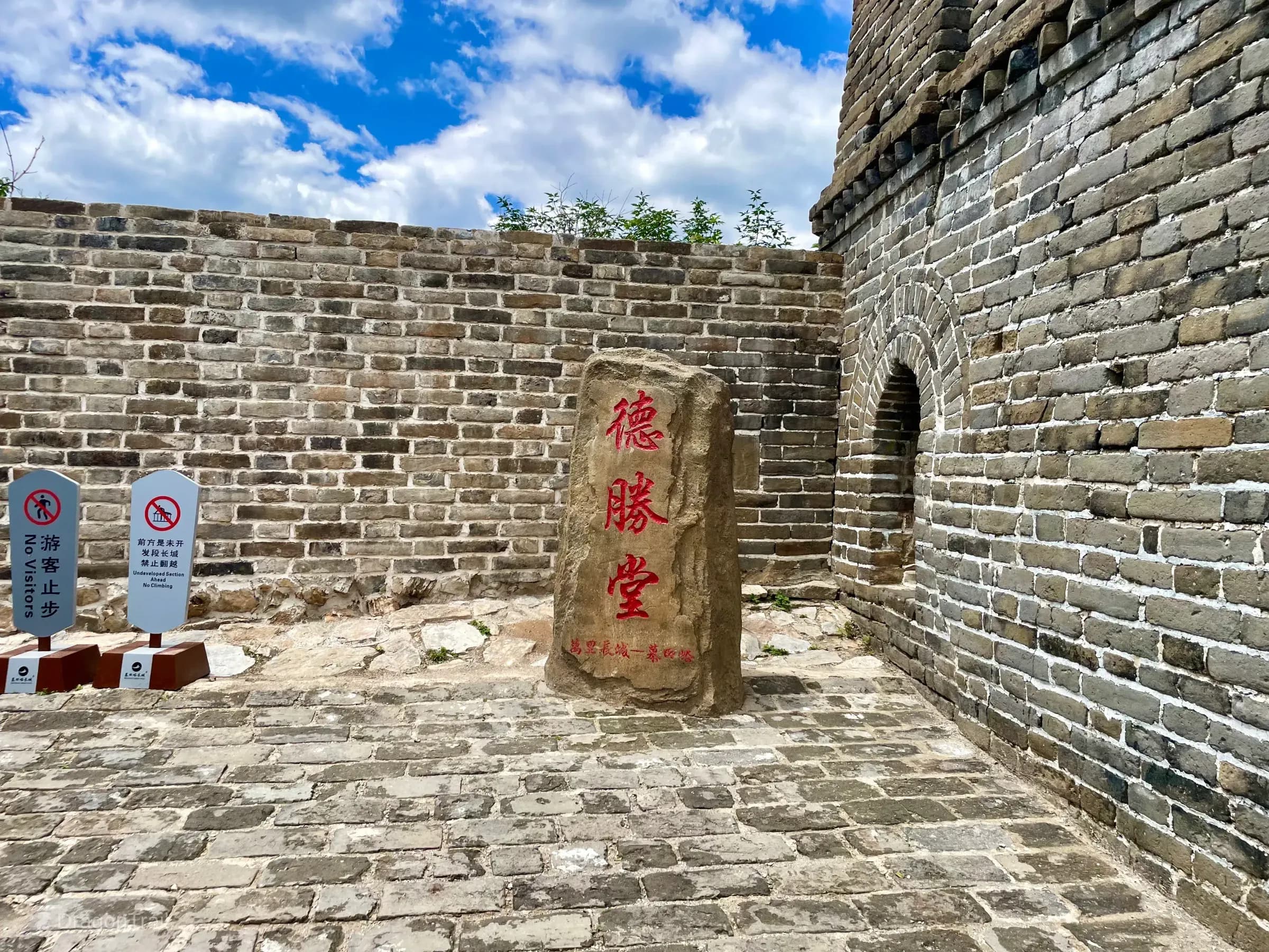Natural stone tablet carved with red Chinese characters 德勝堂 (Desheng Hall) before Mutianyu Tower 23’s arched brick entrance, with No Visitors and Undeveloped Section Ahead signs on the left