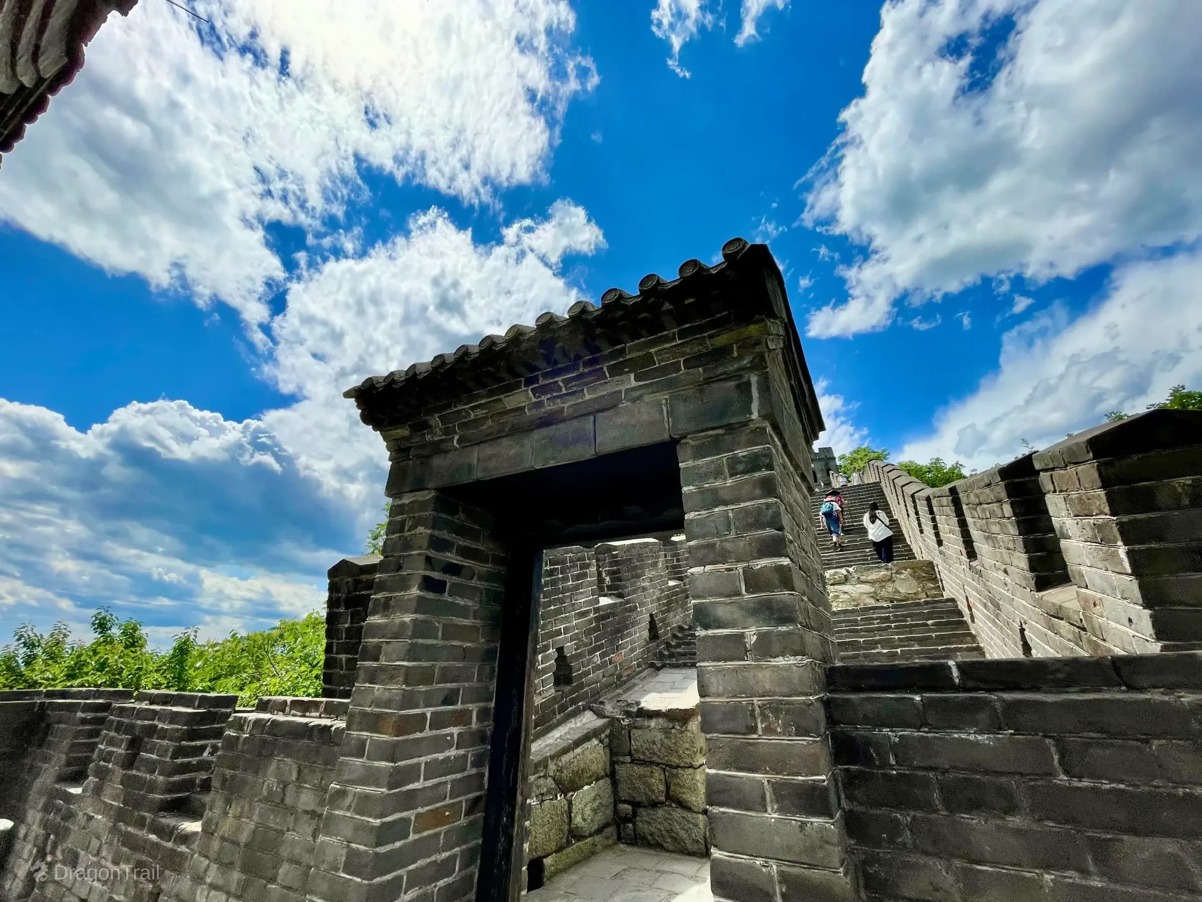 Low-angle view of a tiled brick gateway and steep stone stairs on Mutianyu Tower 4 under blue sky