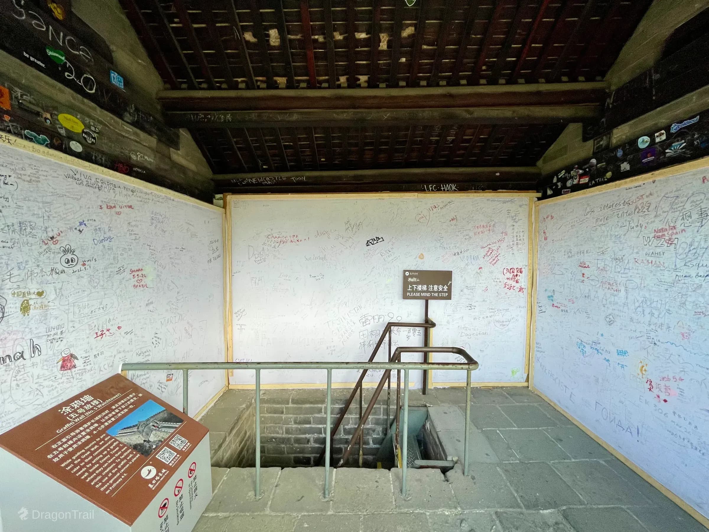 Interior of Mutianyu Tower 5 with white visitor signature boards, stair railing, and graffiti-wall signage