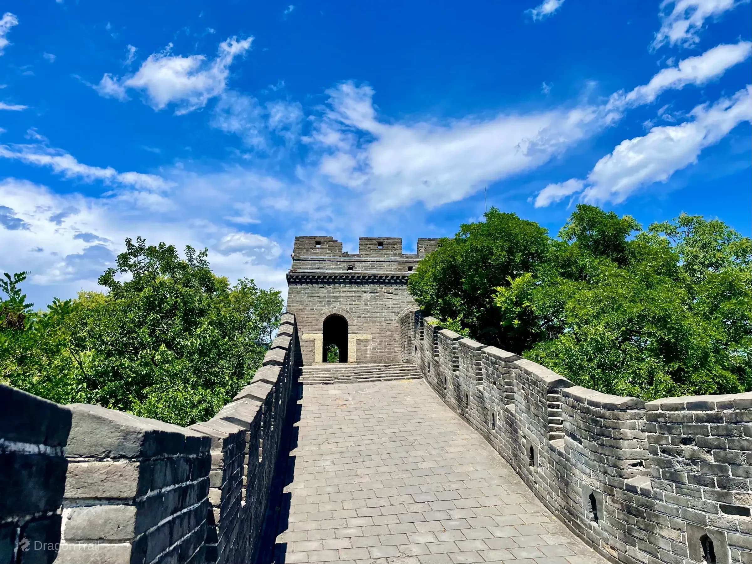 Eye-level Mutianyu wall path of grey pavers leading straight to Tower 7’s single arched entrance under a bright blue cloudy sky