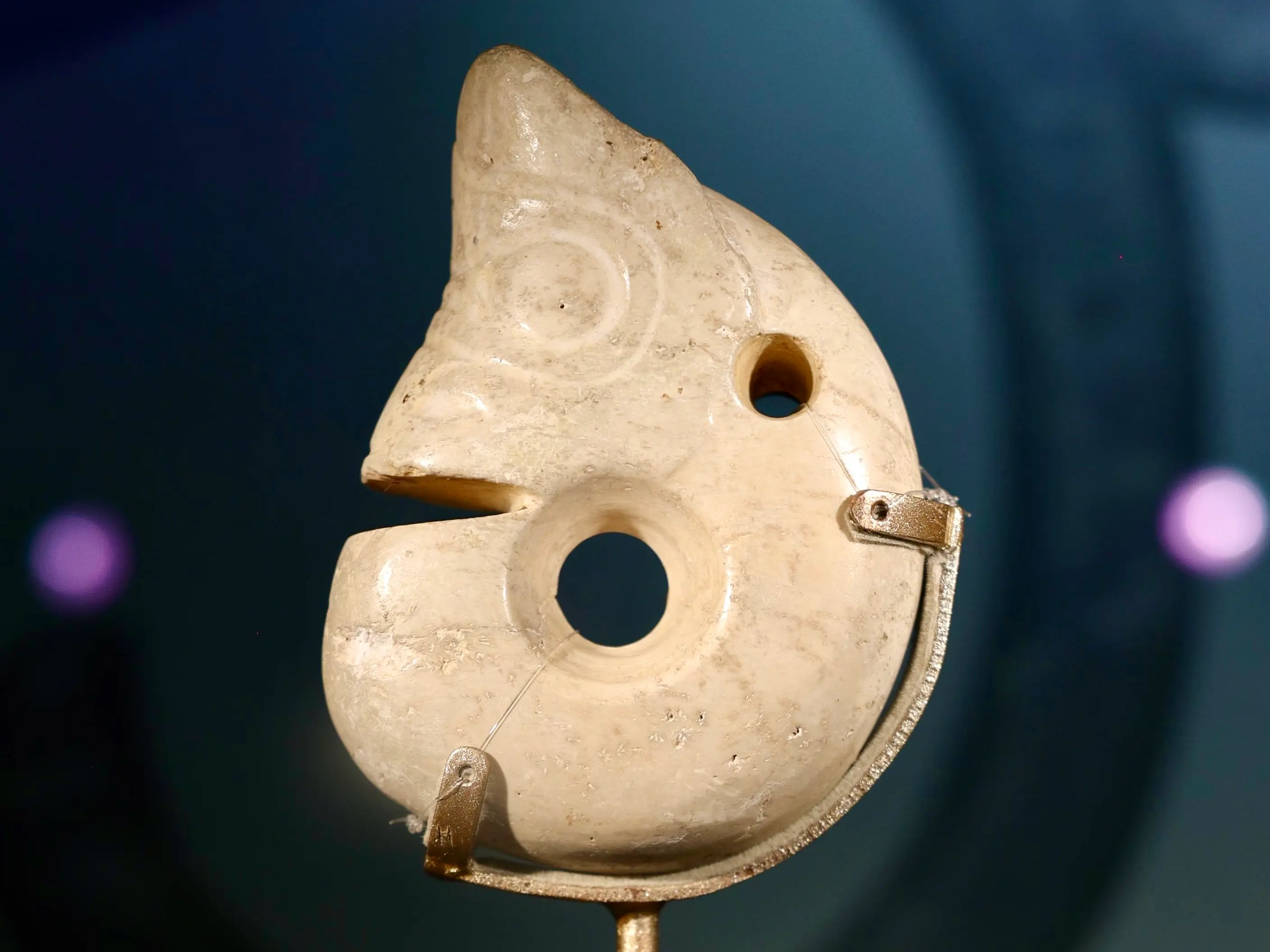 A C-shaped jade artifact with a zoomorphic design, featuring a circular hole and spiral carvings.