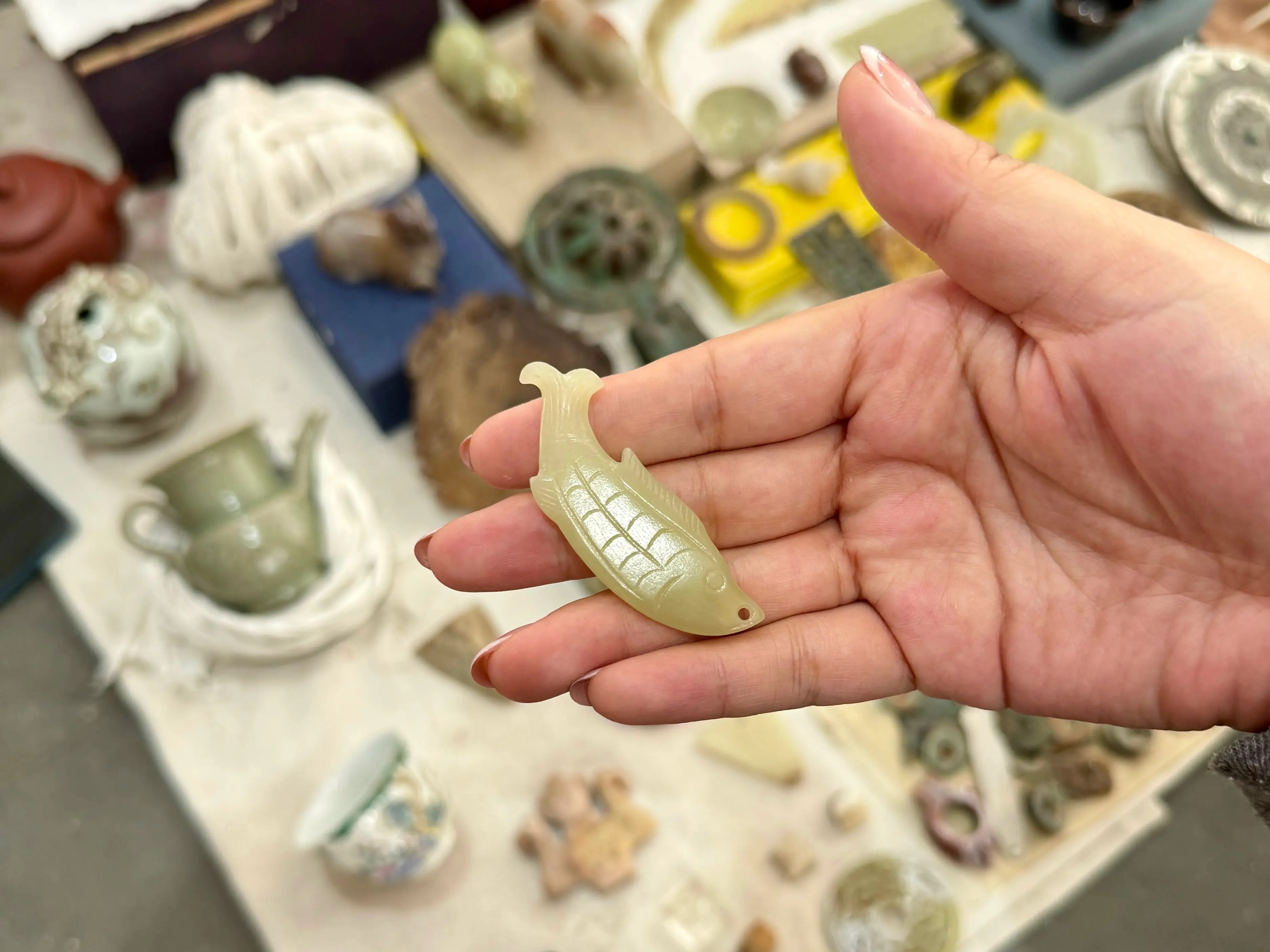 A hand holding a small jade fish pendant with detailed scales