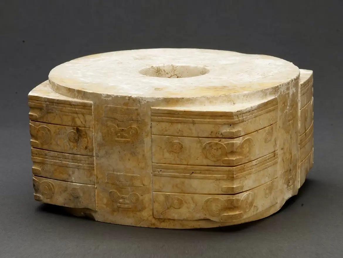 A square-section tube with a circular bore, made of light-colored stone with carved patterns.