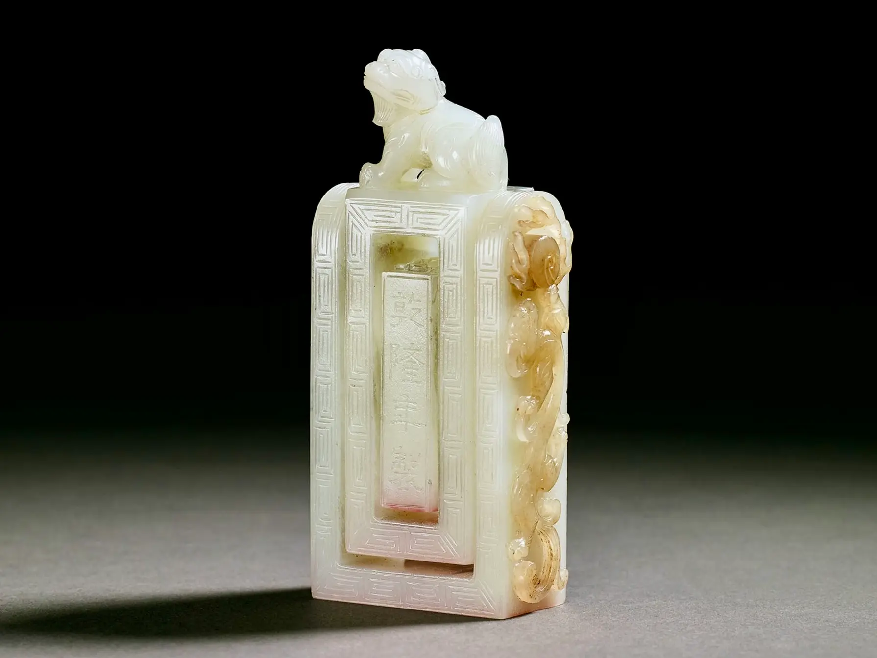 A white nephrite seal with intricate carvings and Chinese characters, topped with a lion figure.