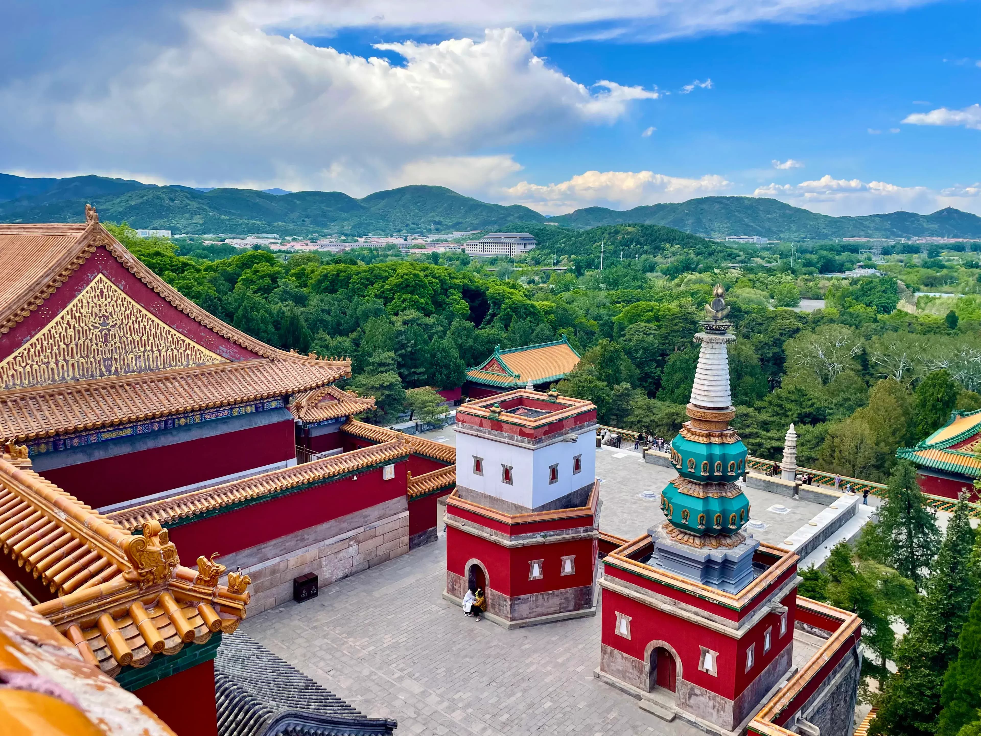 Aerial view of traditional Chinese architecture with ornate roofs and a pagoda-like structure amidst lush greenery.