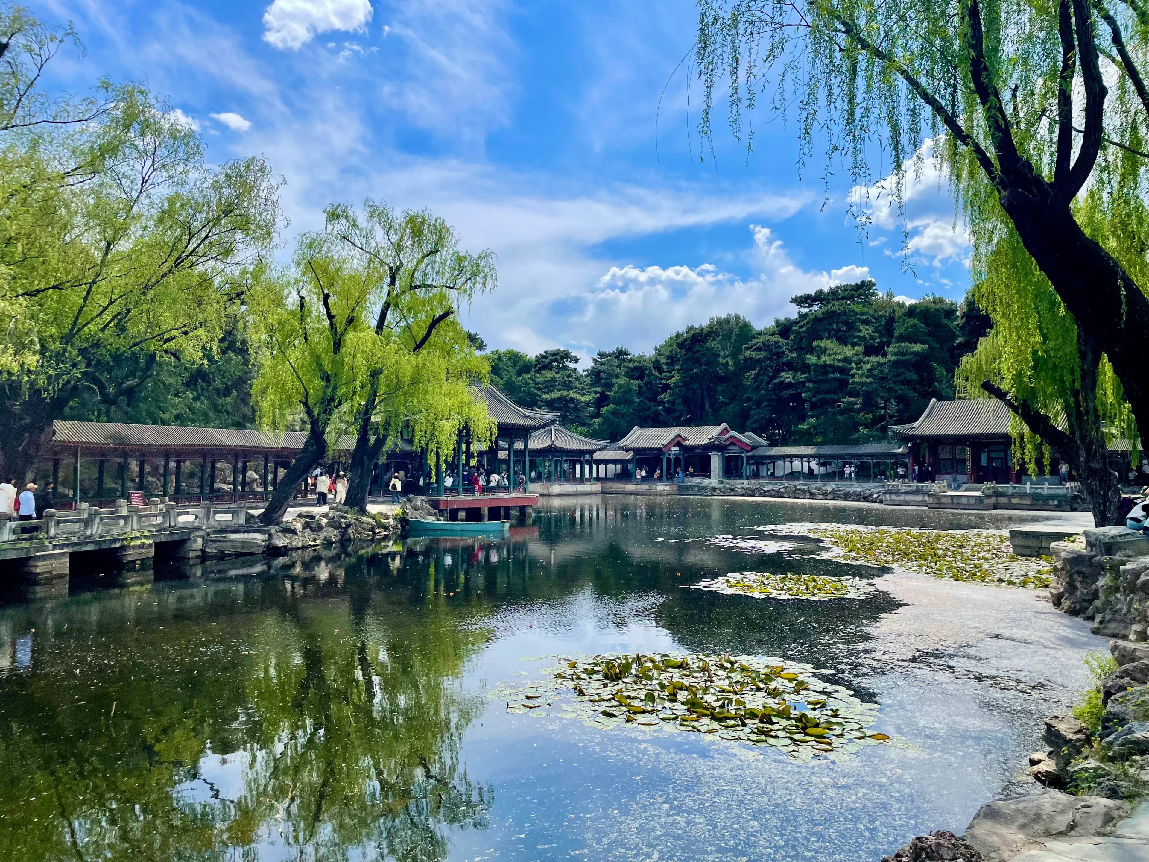 A serene garden scene with a pond, traditional Chinese pavilions, and willow trees.