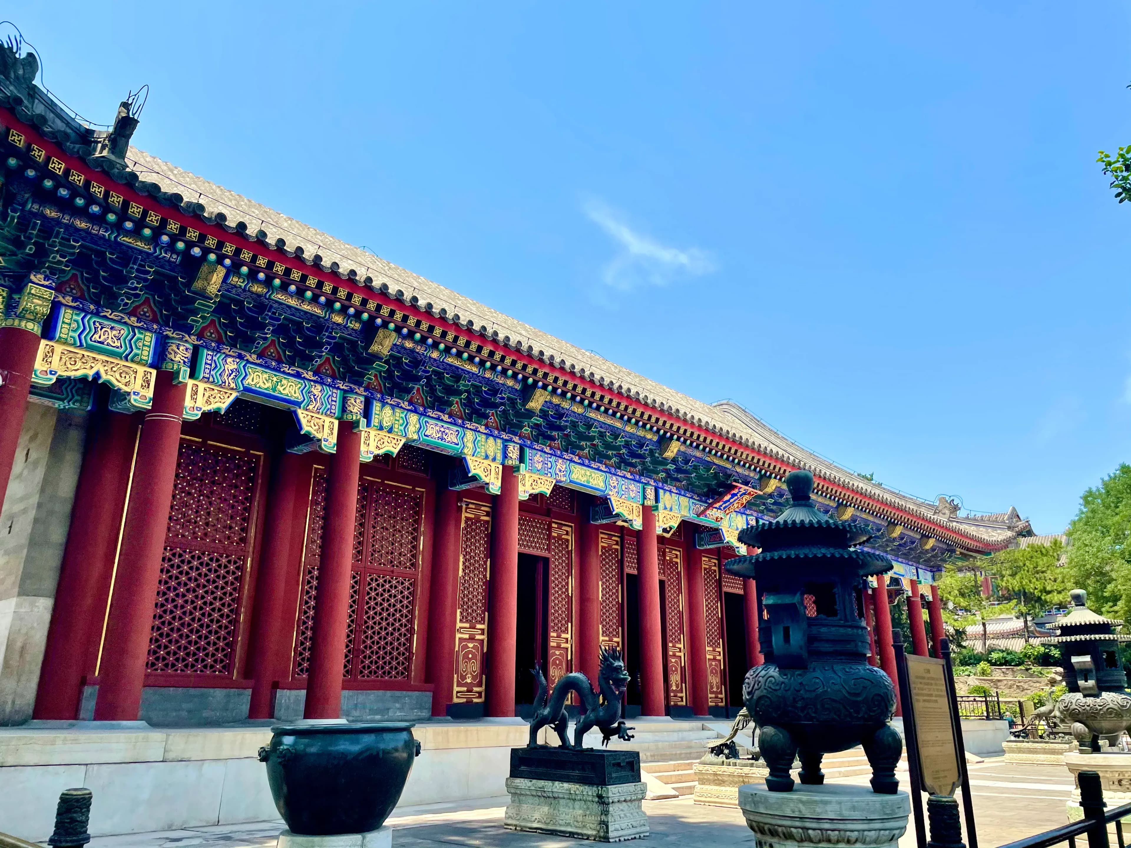 Traditional Chinese building with ornate decorations and red pillars, featuring a dragon statue and incense burners in the foreground.