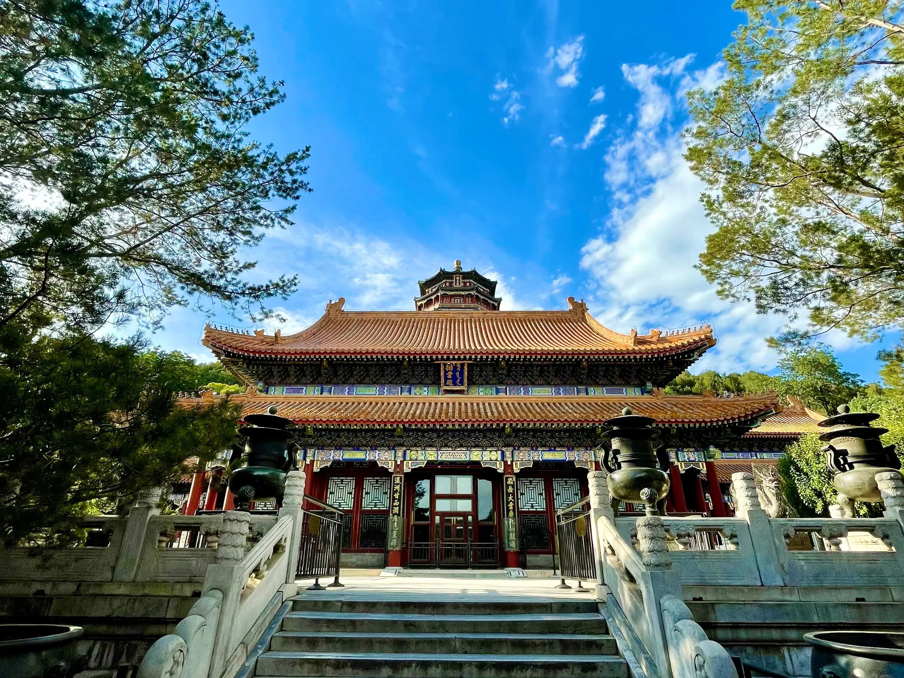 Traditional Chinese architectural structure with ornate roof and stone railings, surrounded by trees under a blue sky.