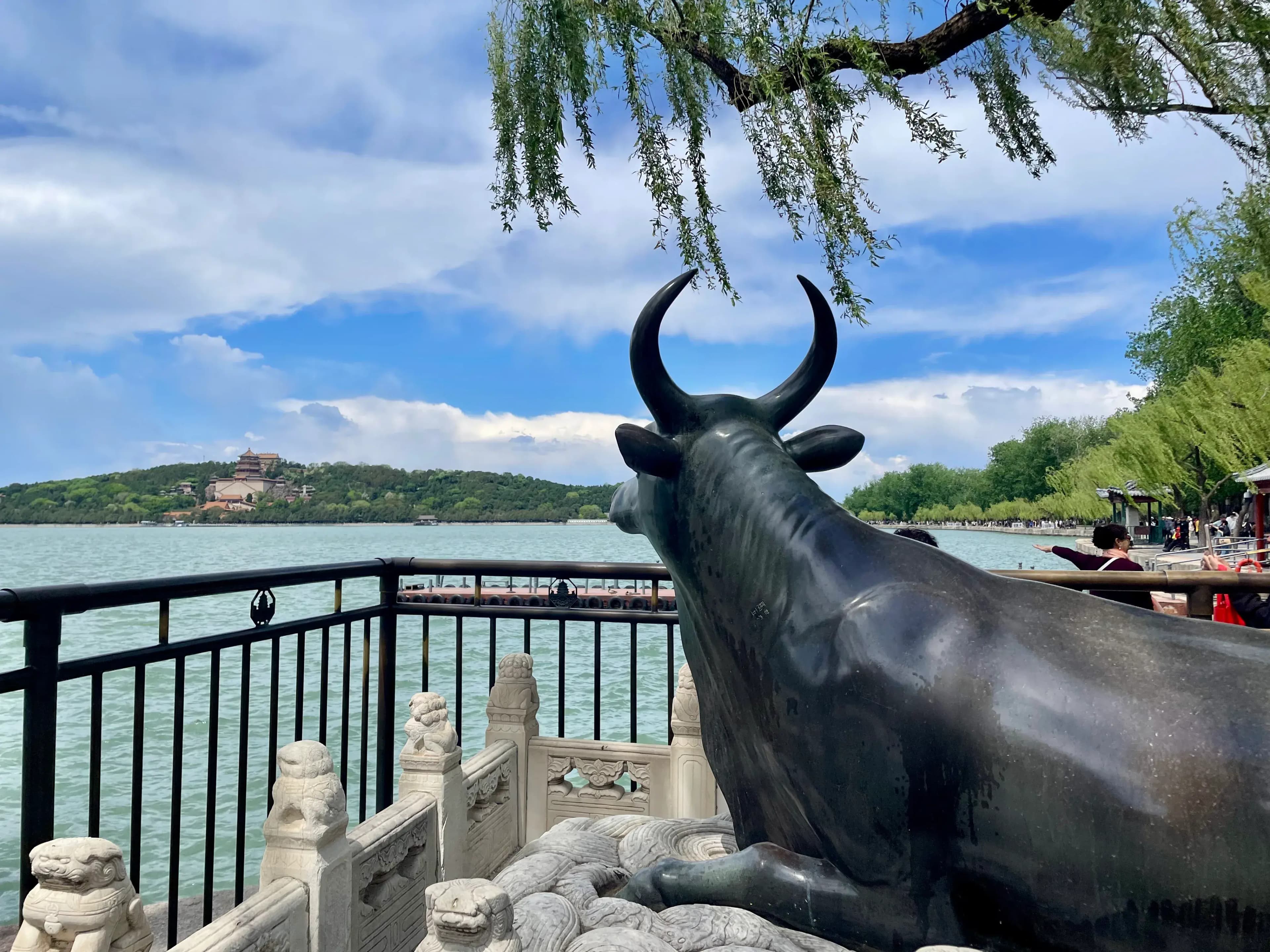 Bronze Ox statue beside Kunming Lake at the Summer Palace with Longevity Hill visible in the background under dramatic clouds in Beijing China