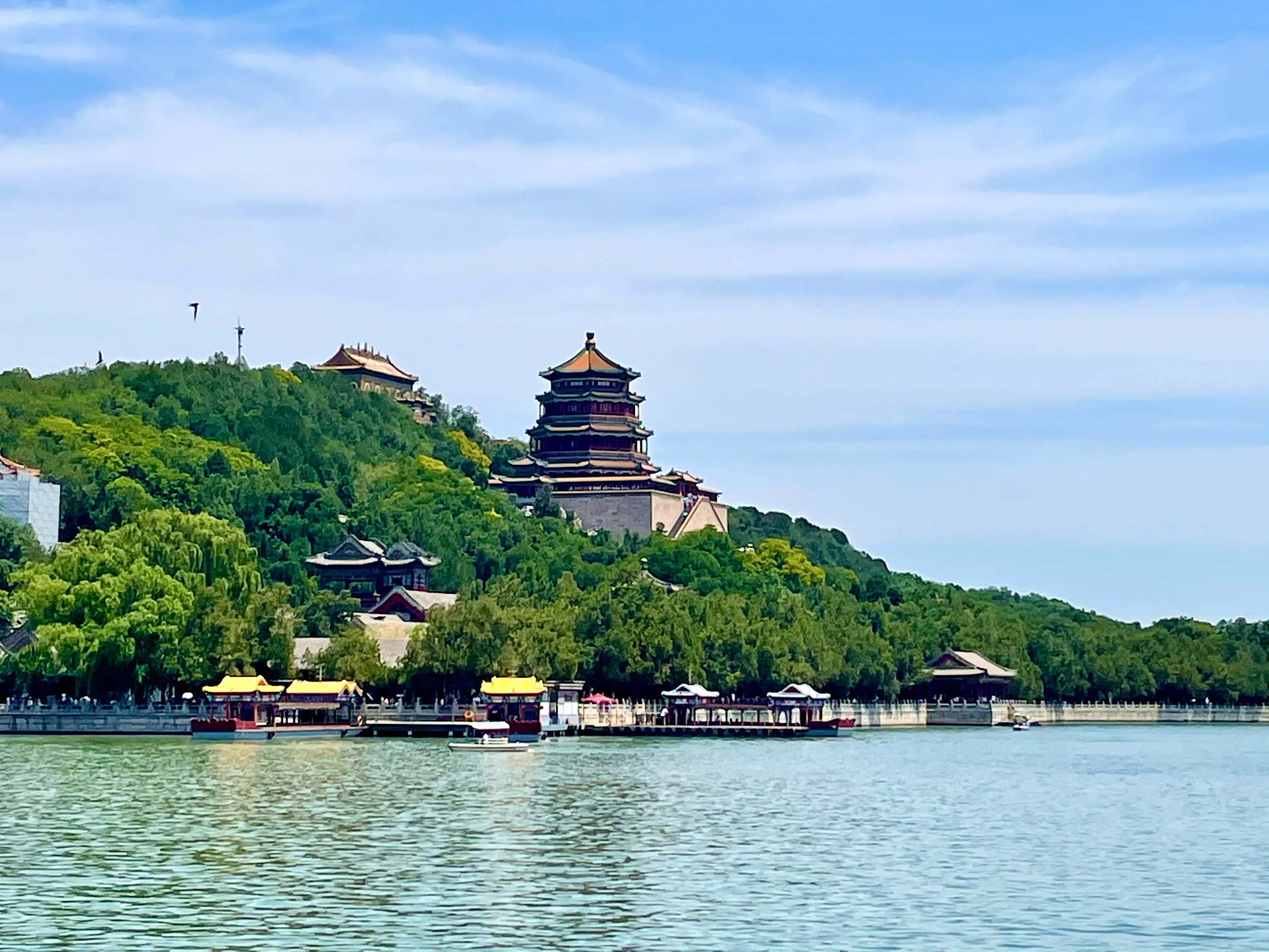 The Tower of Buddhist Incense is seen from across a body of water, surrounded by lush green trees and traditional Chinese architecture.