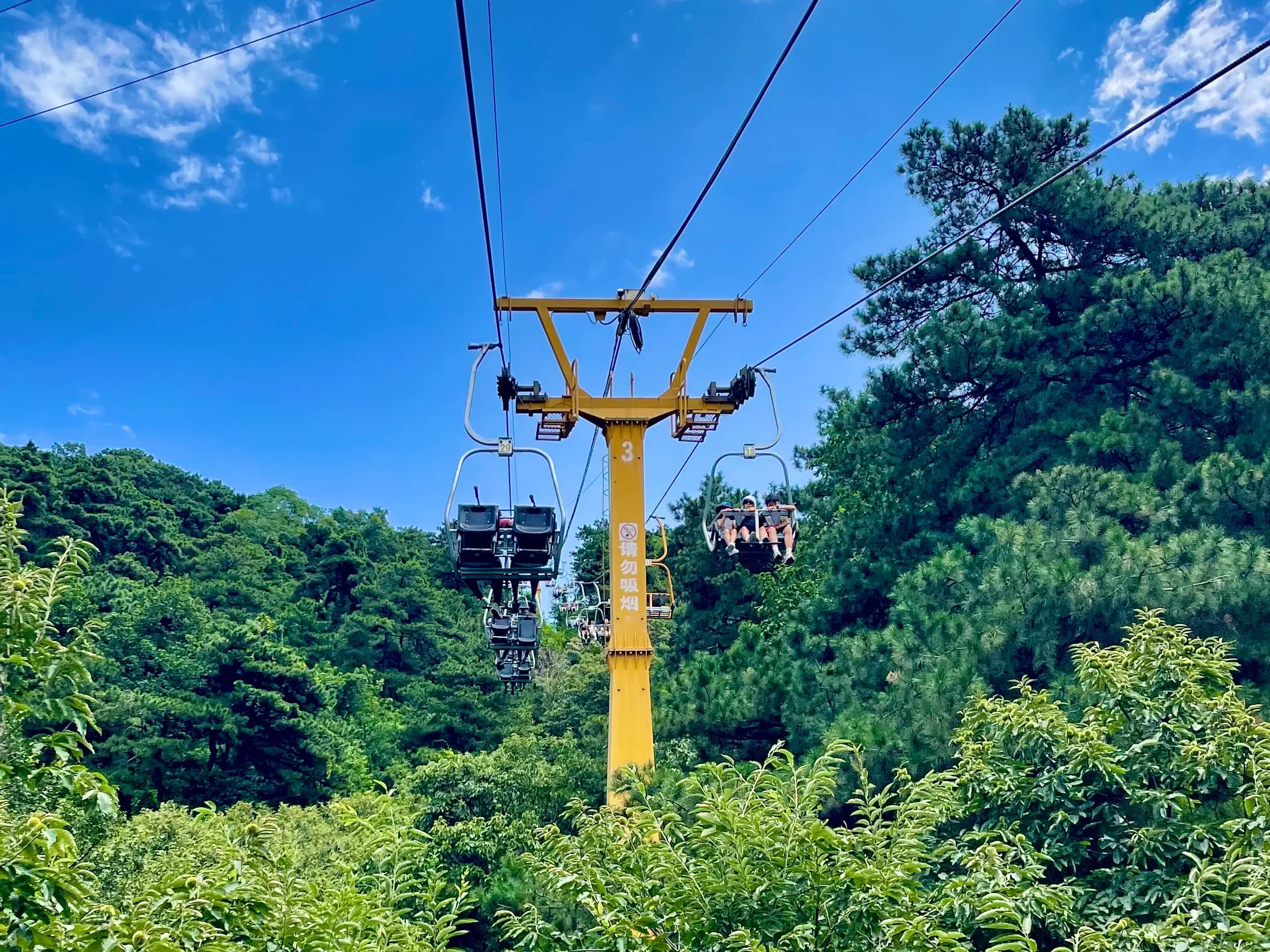 Open chairlift at Mutianyu Great Wall carrying visitors above green forest toward the east route.