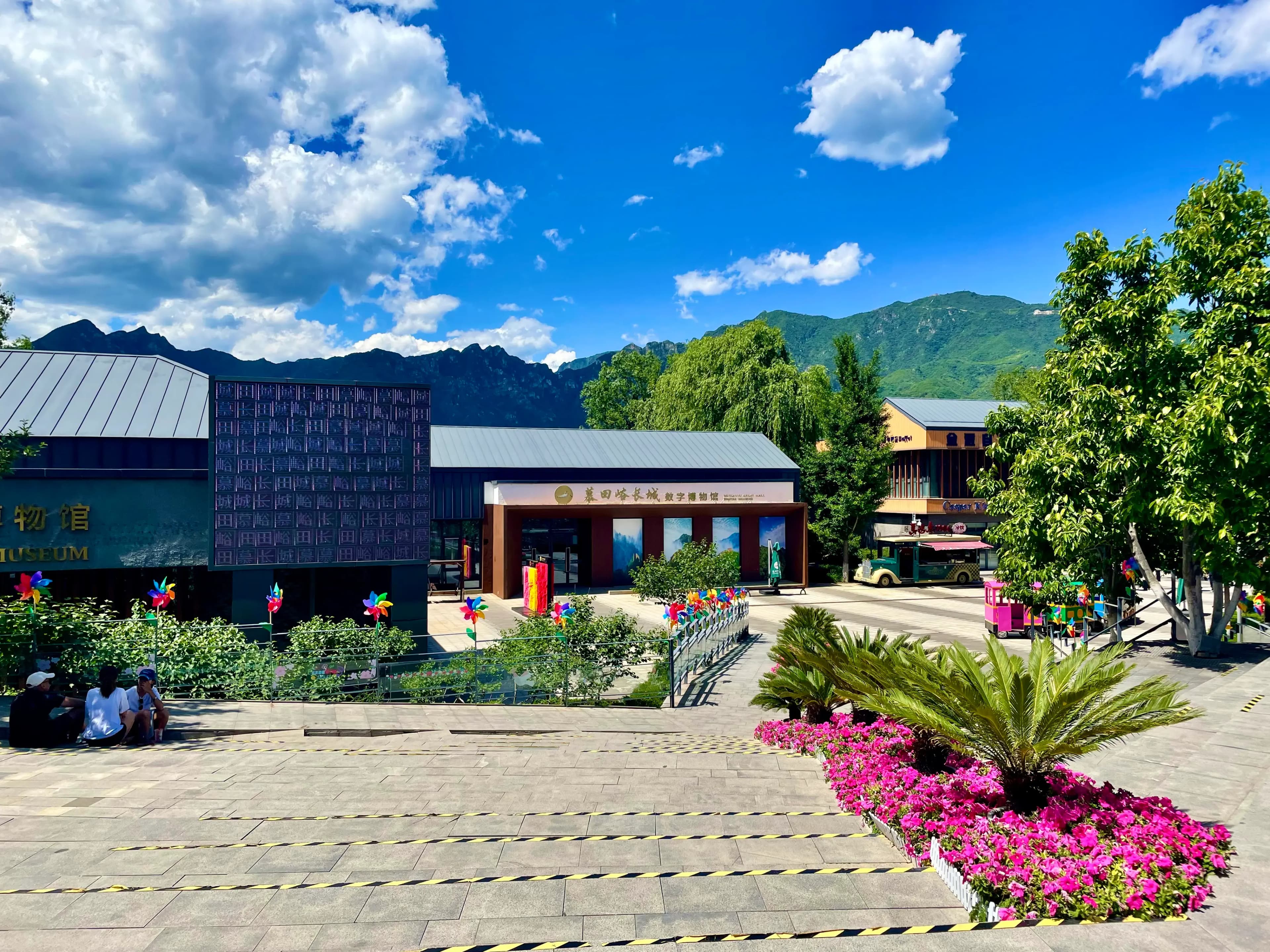Exterior of the Mutianyu Digital Museum, now operating as The Epic Great Wall XR Experience Space, with the Mutianyu ridges rising behind a sunlit plaza near the scenic area.