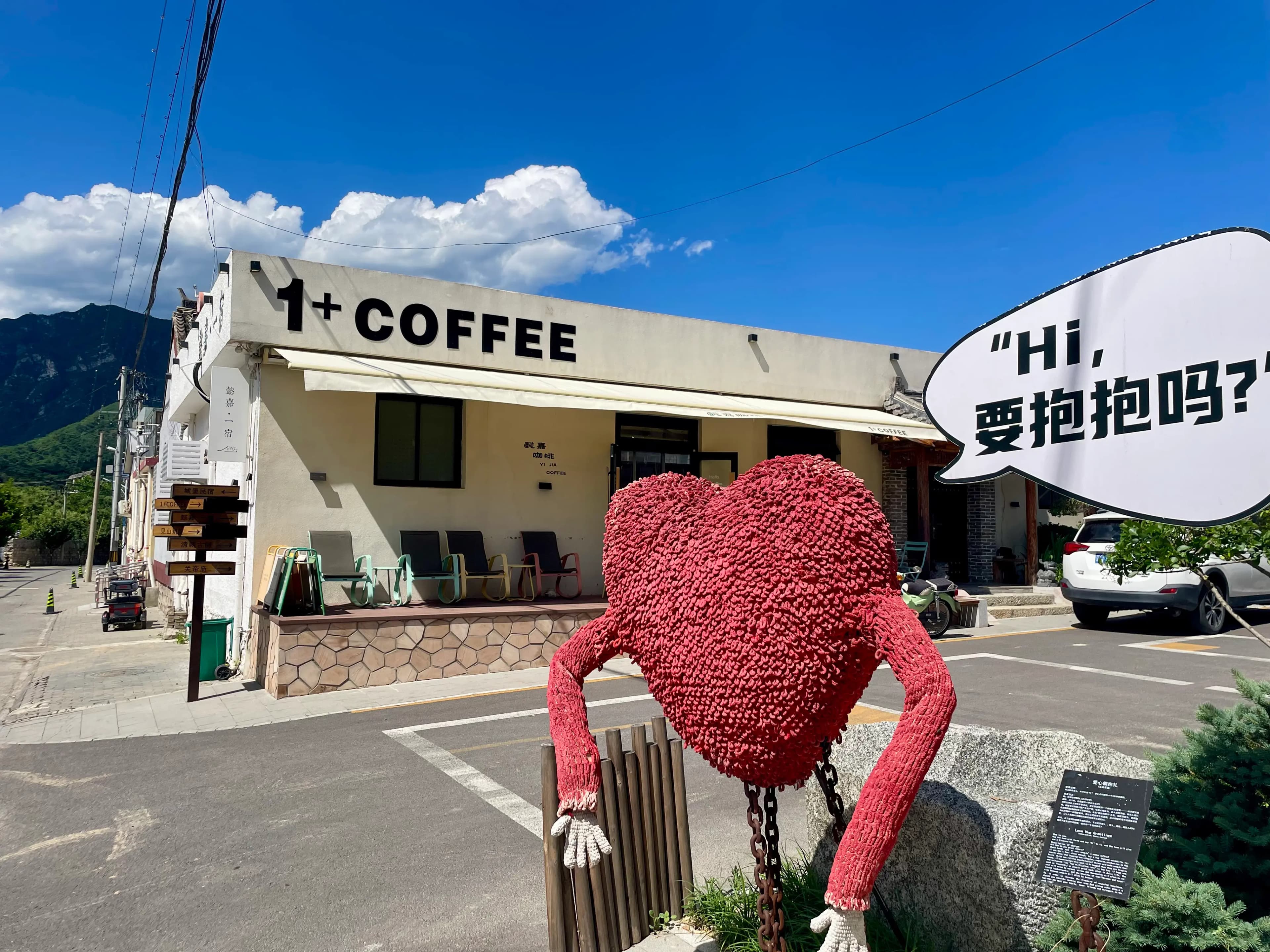 A design-led café in Xinying village near Mutianyu, with a white archway, “COFFEE” signage, and a red art figure outside, illustrating Xinying’s art-village transformation as a quieter overnight base than the Mutianyu gate area.