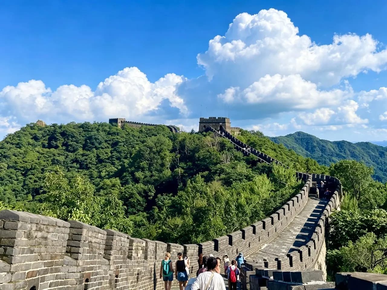 Mutianyu Great Wall in summer with restored watchtowers, green mountains, and a blue sky with clouds.