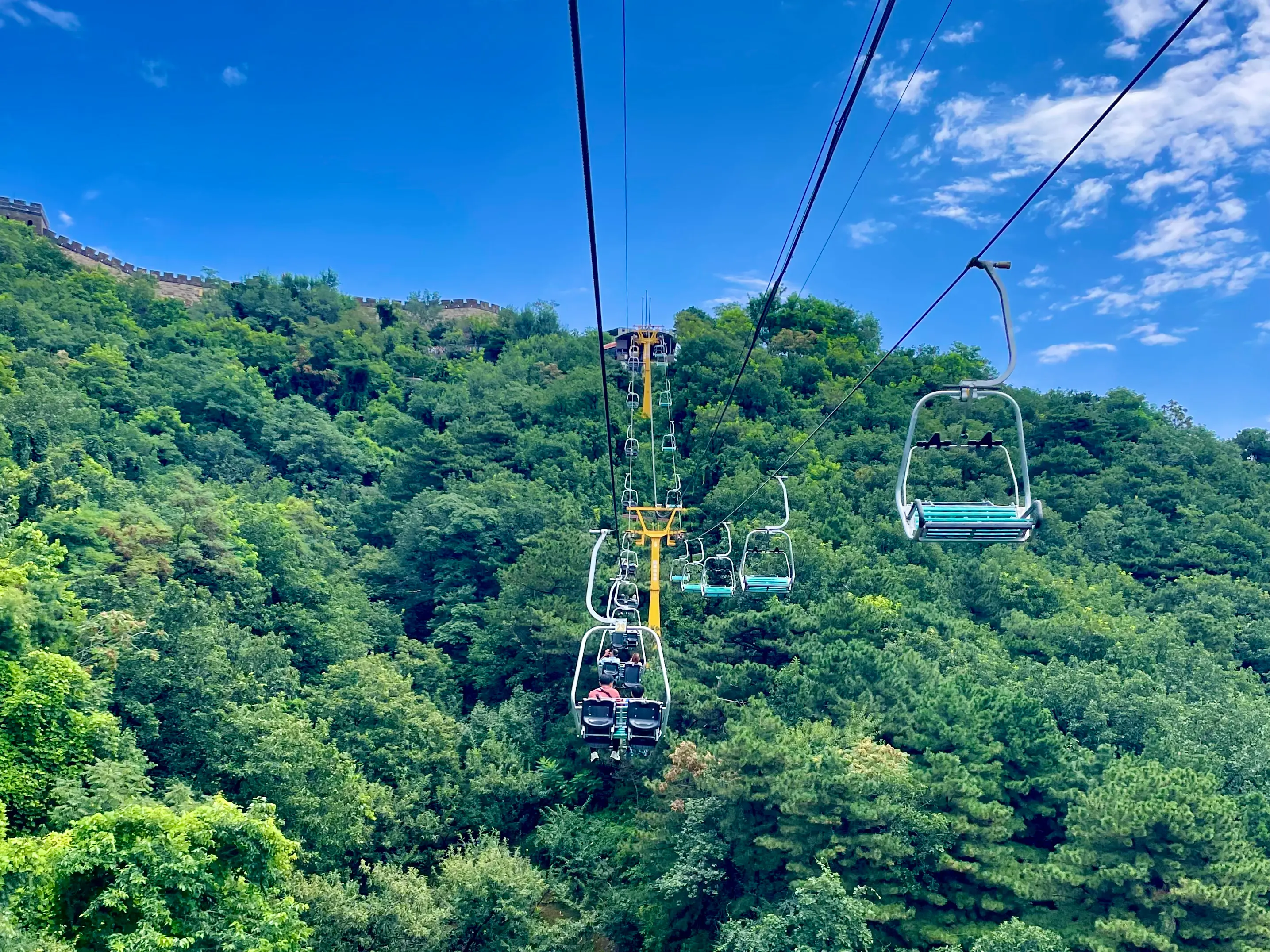 Chairlift ascending toward the Mutianyu Great Wall east route with watchtowers visible above the green hillside.