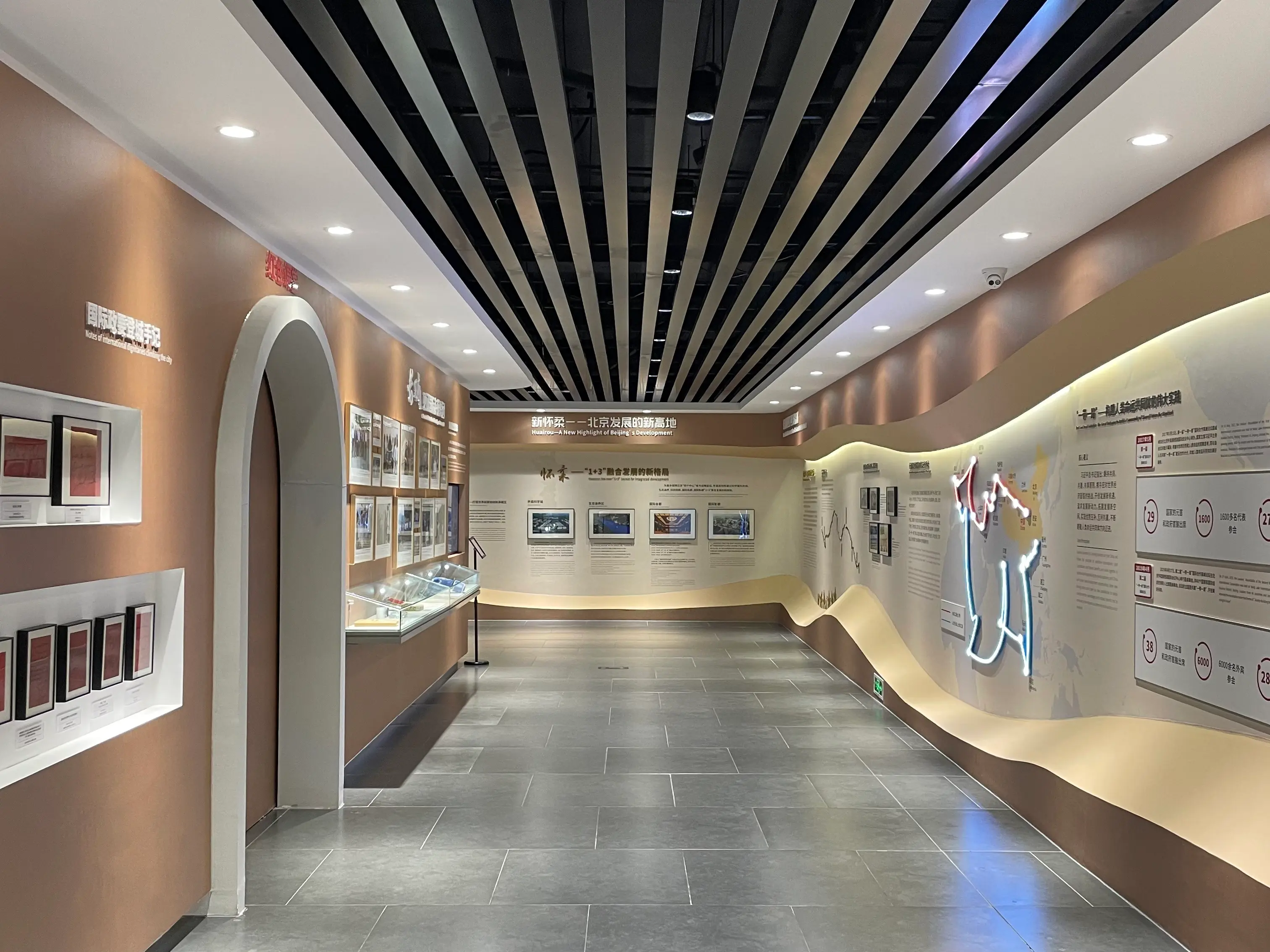 Interior corridor of Mutianyu's Great Wall Spirit Exhibition Hall, with bilingual exhibition panels, framed displays, and a curved wall-mounted timeline showing the historic role of the Great Wall.