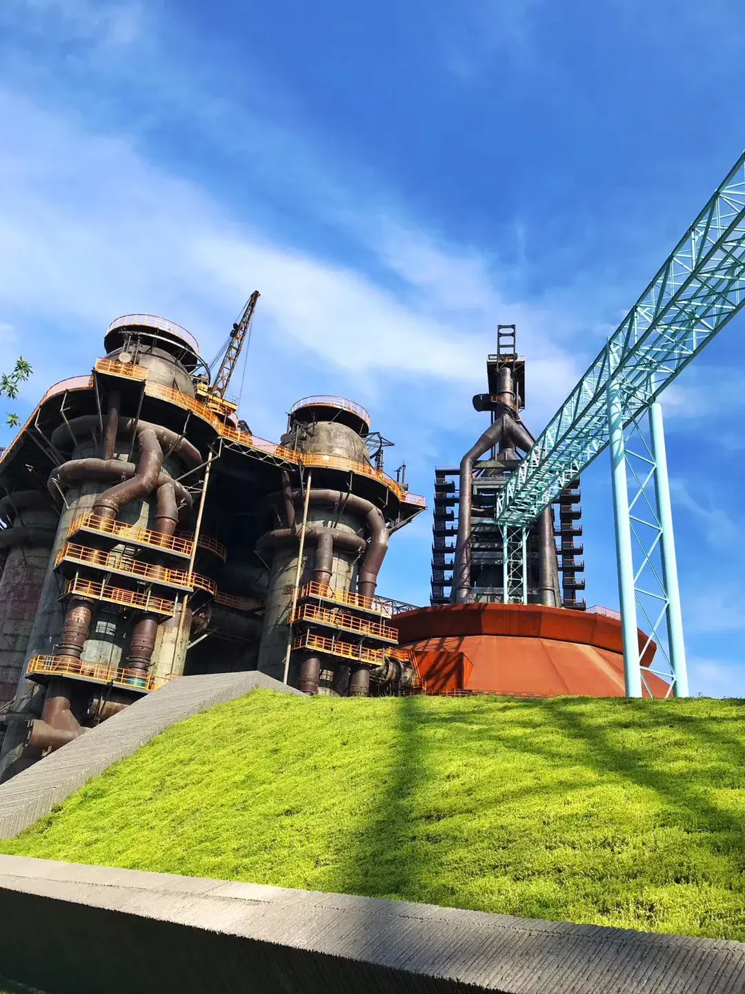 Low-angle view of twin blast furnaces and a light-blue lattice gantry above a grassy slope at Shougang Park, Beijing