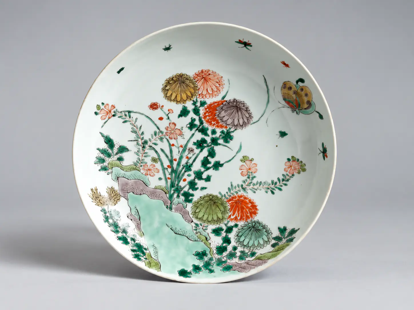 Un plato de porcelana decorado con flores y mariposas coloridas