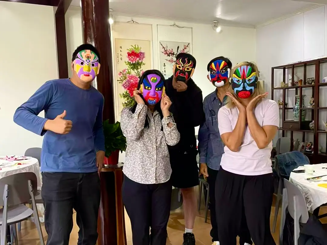 Five people wearing colorful opera masks standing indoors