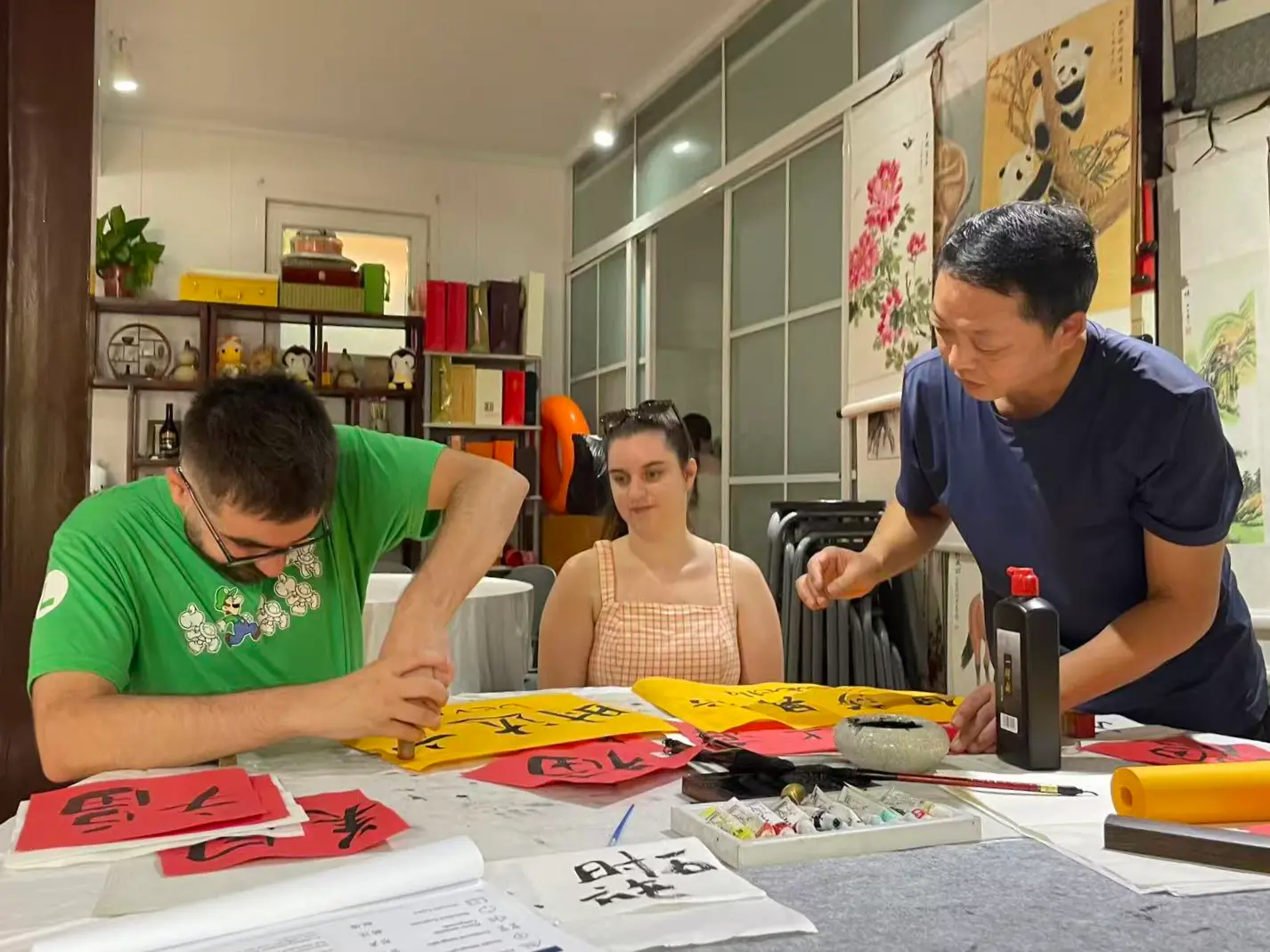 People practicing calligraphy with red and yellow papers on a table.