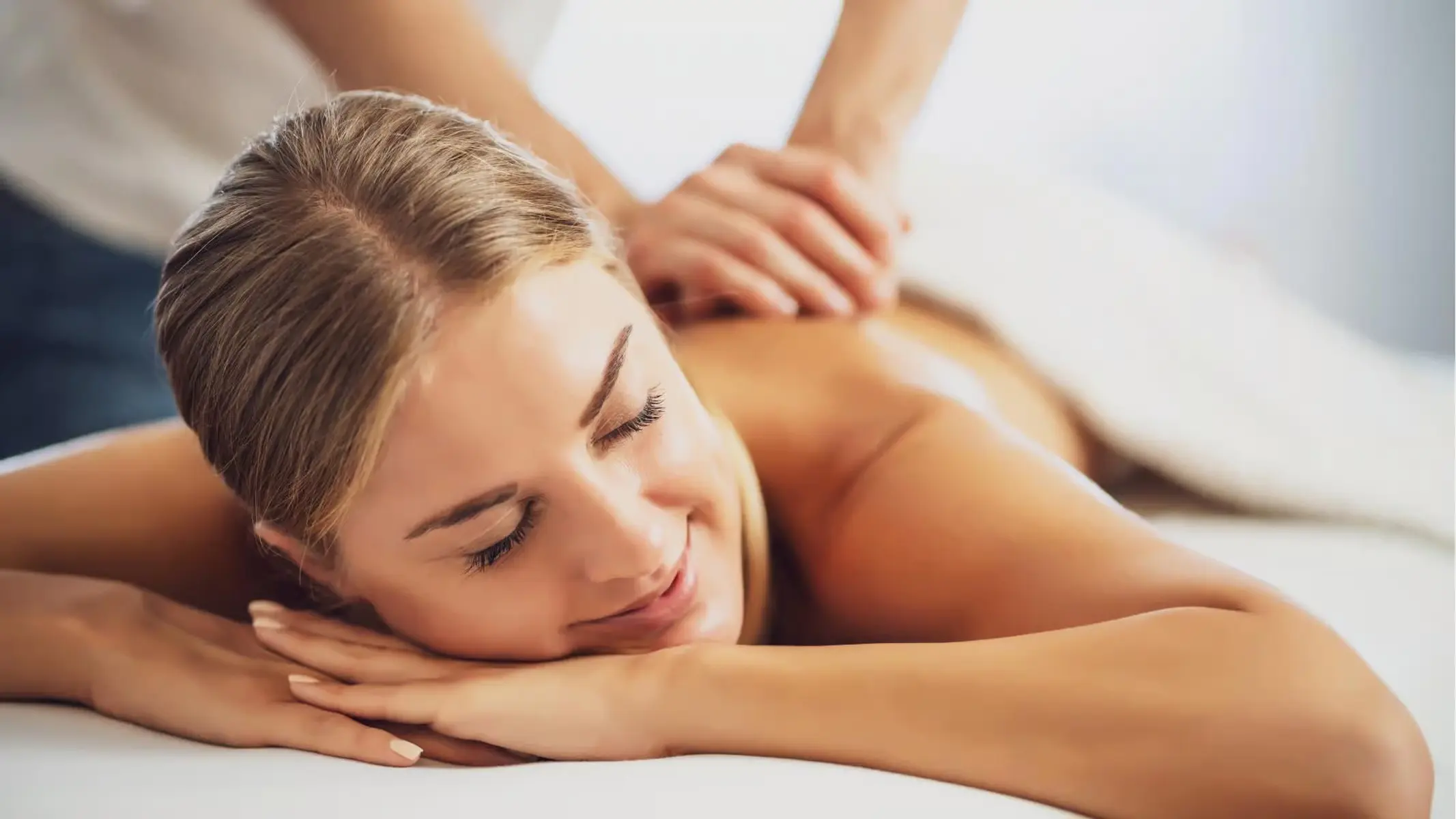 A woman lies face down on a massage table while a therapist massages her back.